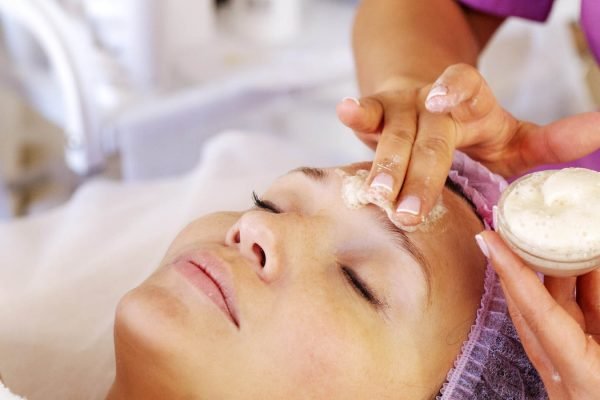 Cosmetologist applies  a moisturizing mask on female face. Woman in a spa salon on cosmetic procedures for facial care.  White woman getting beauty treatment therapy.